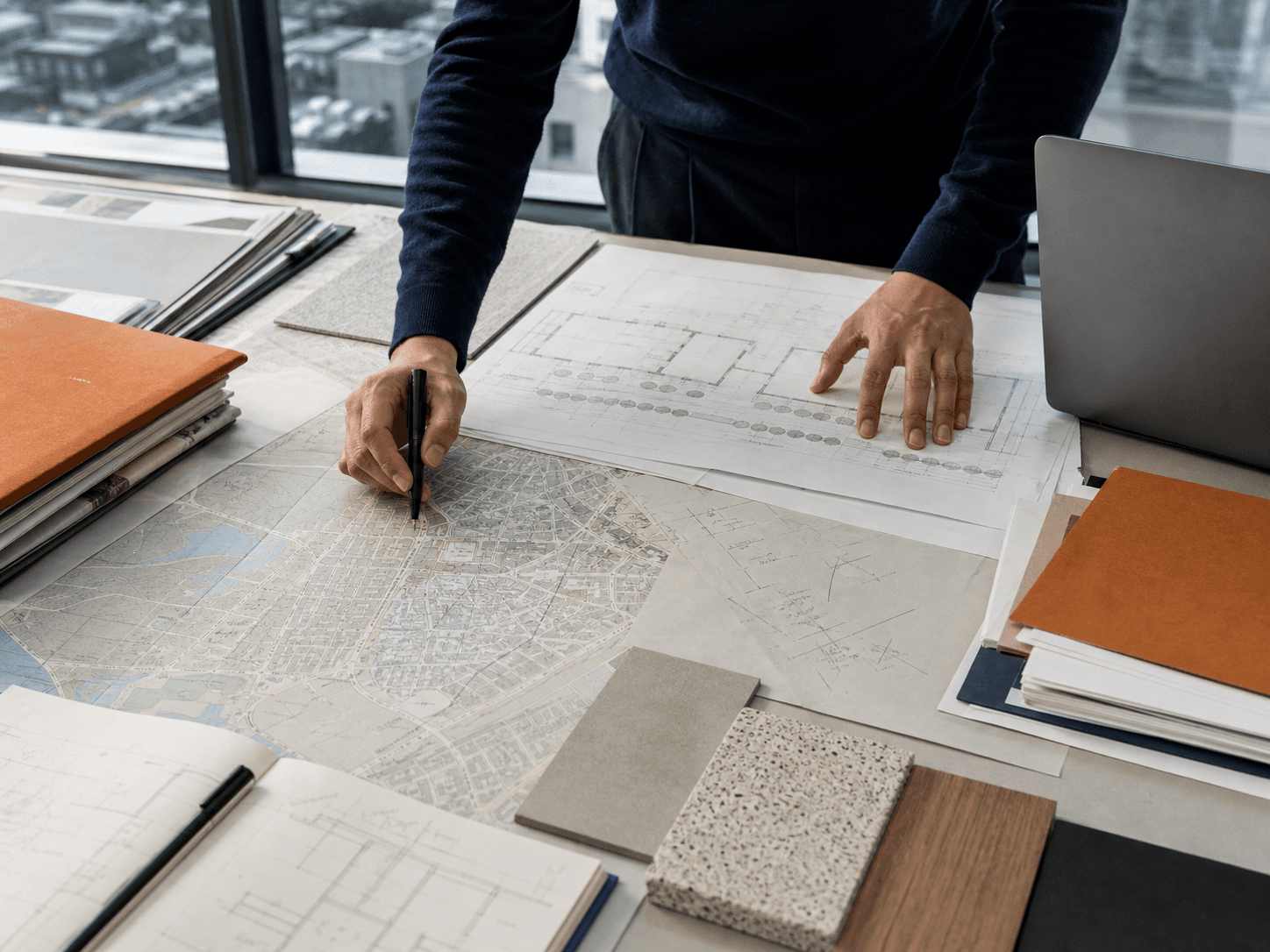 A researcher reviewing architectural plans and a city map at a planning desk.